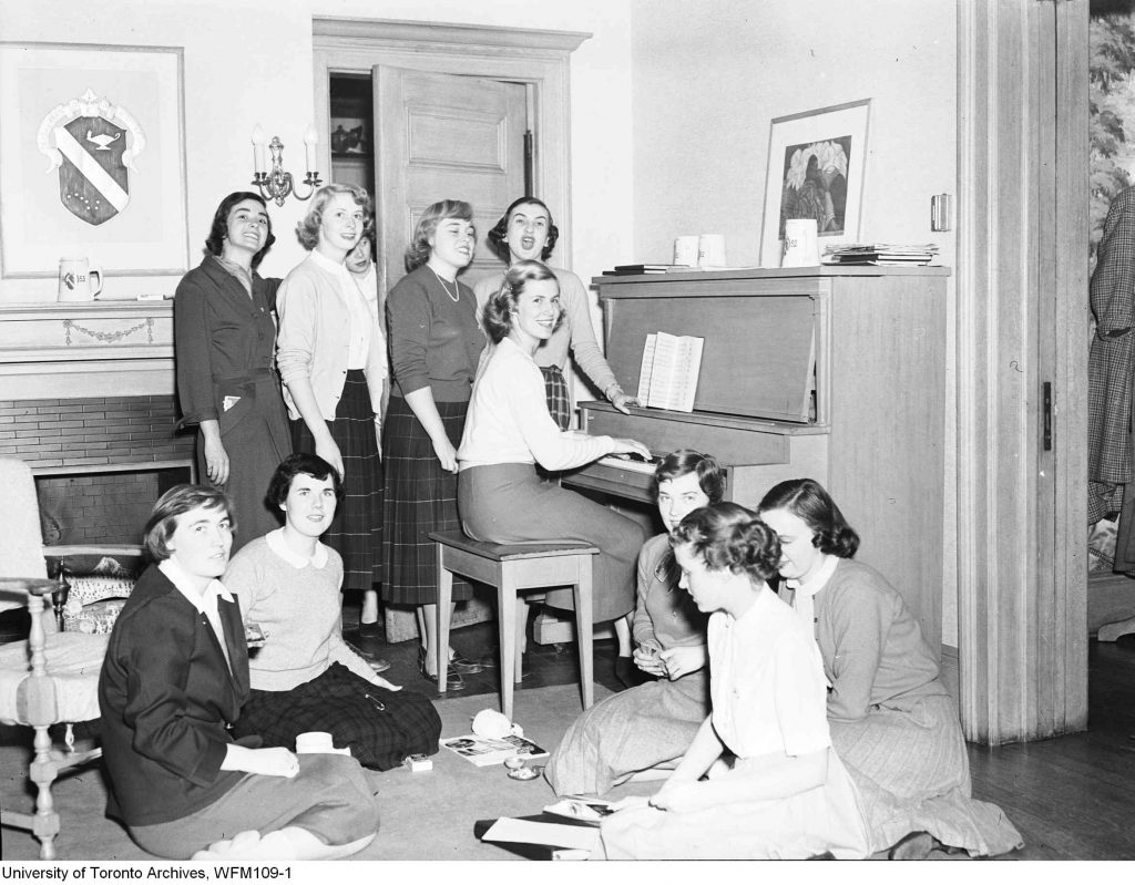 1950s vintage photo: University of Toronto-Alpha Phi Fraternity - women members singing at the piano (1952) in 1950s fashions. 