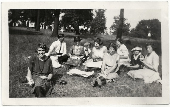 1920s vintage photo of a group of people in 1920s fashions enjoying a picnic in a park. 