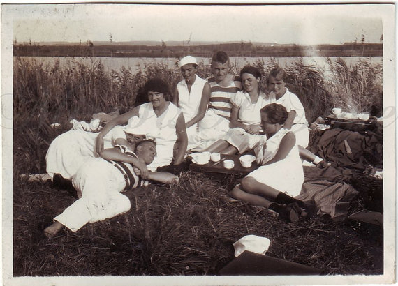 1930s vintage photo of a group of men and women having a picnic by the lake all dressed in white. 