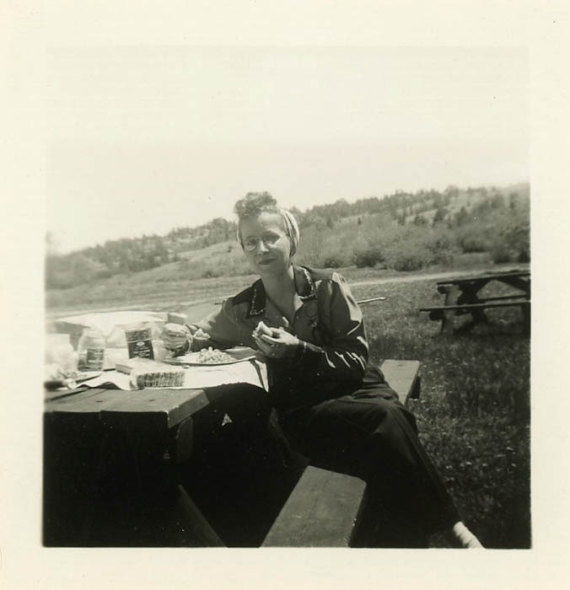 1940s vintage woman eating food at a picnic. She is wearing a western style shirt and looks like a 1940s turban style on her head. 