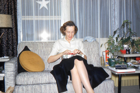 1950s photo of a woman on a couch wrapping a christmas present