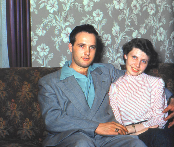 1950s photo of a young couple on a couch in 1950s fashions. 