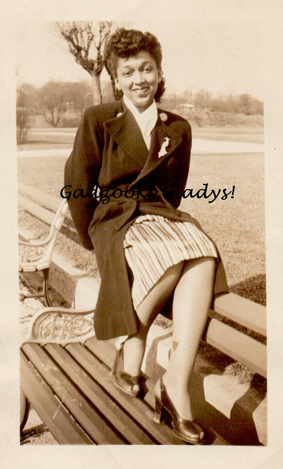 1940s vintage photo of a pretty young Black woman wearing a jacket with a peacock brooch and peep toe shoes. Fantastic 1940s hairstyle and 1940s fashion.