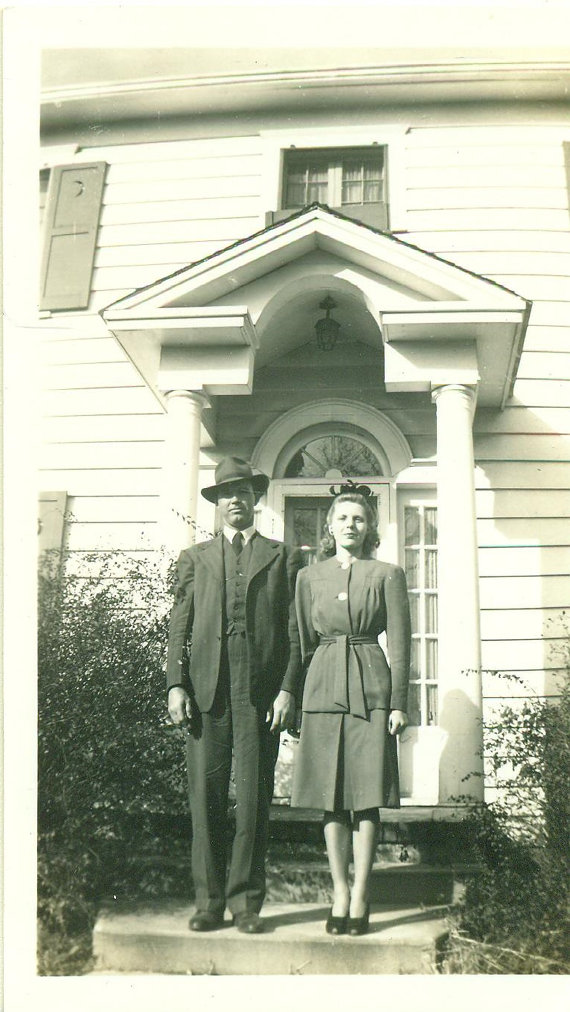 1940s vintage photo of a couple in 1940s fashions posing in front of their house. 