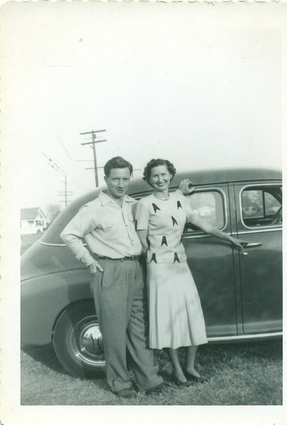 1940s vintage photo of a couple posing in front of a car wearing 1940s fashions.