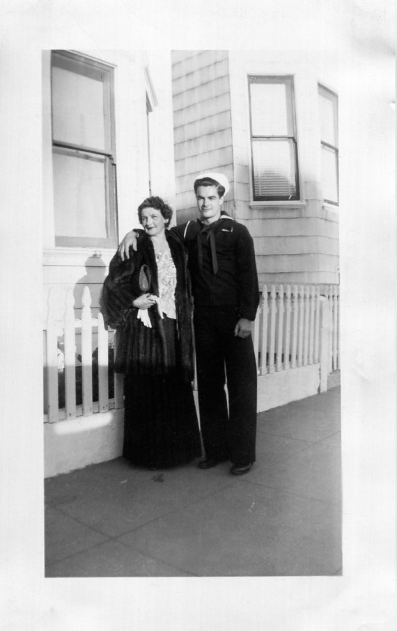 1940s image of sailor with his mother posing together. The mother is all dressed up in eveningwear. 