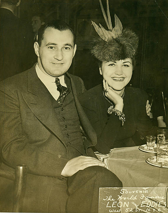 1940s vintage photo of a couple in a restaurant. The woman is a wearing a 1940s hat with a bird in it. Fun 1940s fashion.