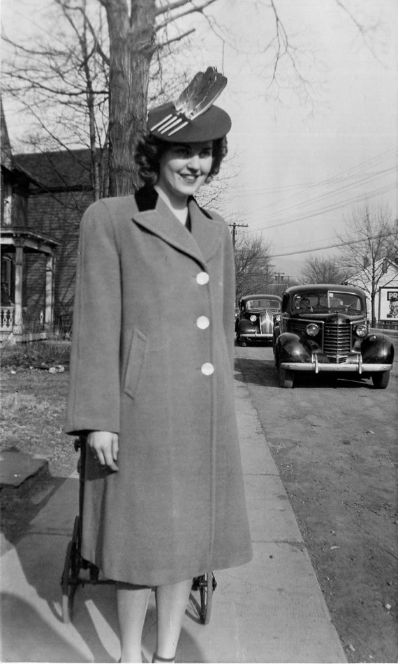 1940s vintage photo of a stylish woman in a 1940s coat wearing a 1940s hat with feathers in the hat. 