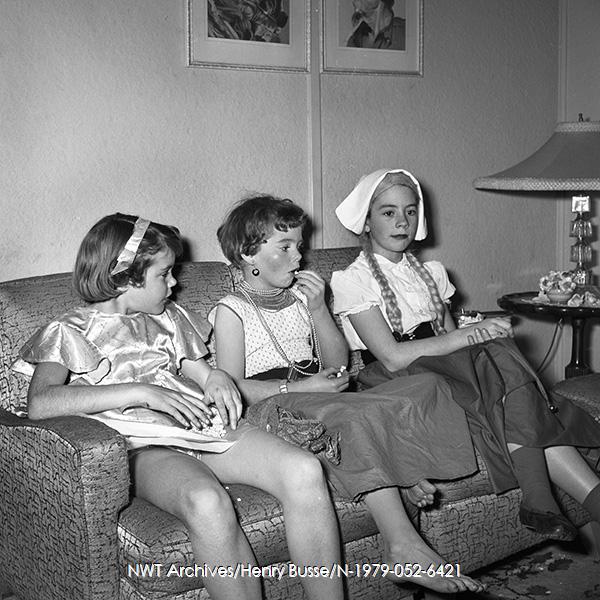 1950s vintage photo of a 1955 vintage photo of 3 girls in halloween costumes sitting on a couch together. 