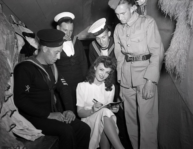 1940s vintage photo of a woman performing from the Marcus Dance showing signing autographs in her 1940s dress and 1940s hairstyle for the sailors in Halifax, Nova Scotia. 