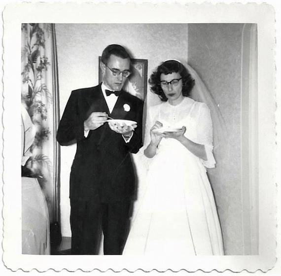 1950s vintage wedding photo of a bride and groom wearing glasses and eating wedding cake