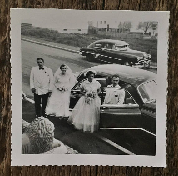 1950s vintage wedding photo of a bride and groom and their wedding party arriving in a 1950s car. 