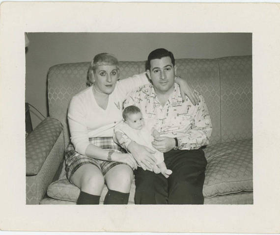 1950s vintage photo of a man and wife holding their baby posing for a picture on the couch. 