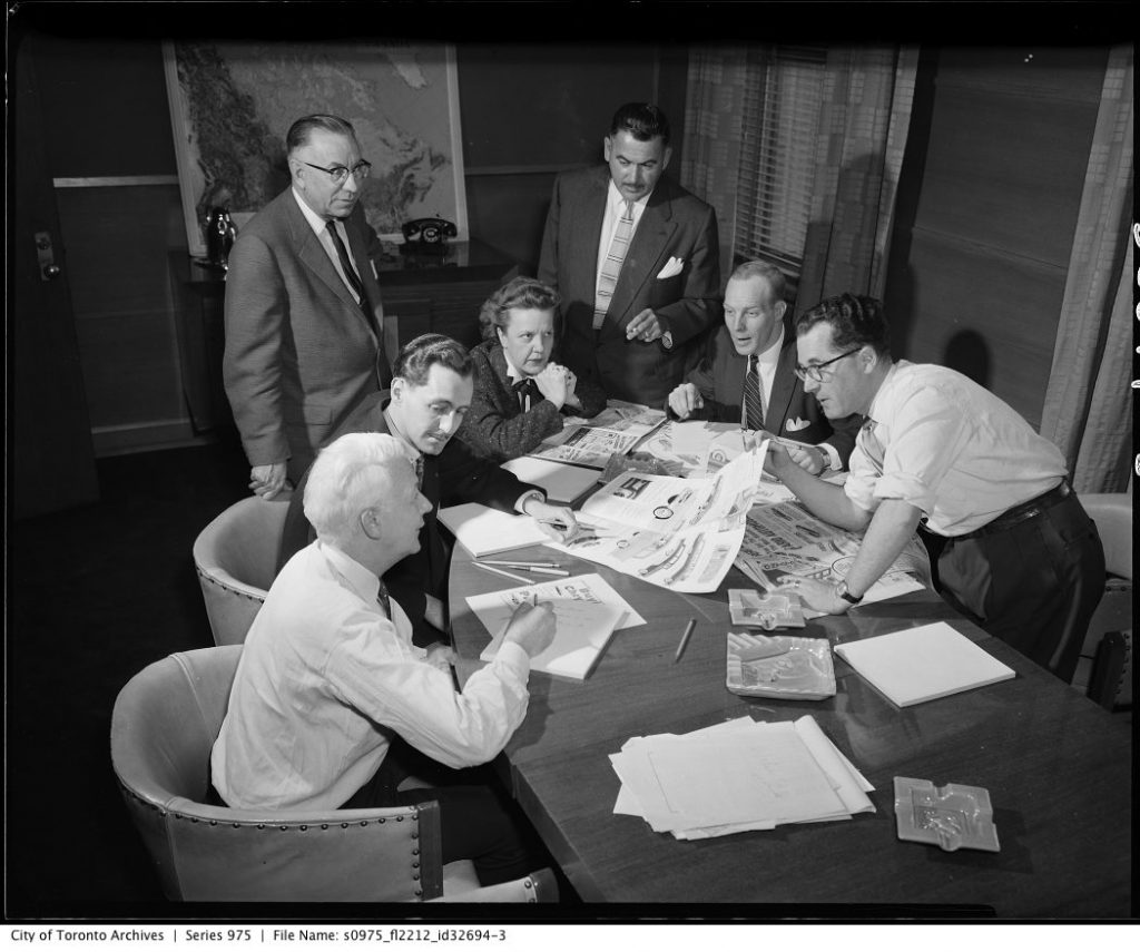 1950s vintage photo consists of two photographs showing a group of men and a woman looking over brochure designs of cars.