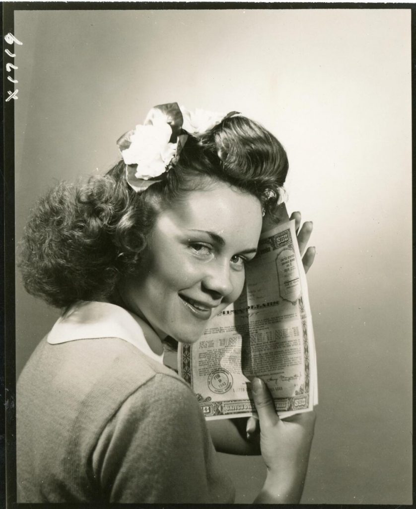 1940s Vintage Photo of a Woman holiday a savings bond. She is wearing a 1940s Hairstyle with a hair flower in her hair. Super vintage hairstyle inspiration. 