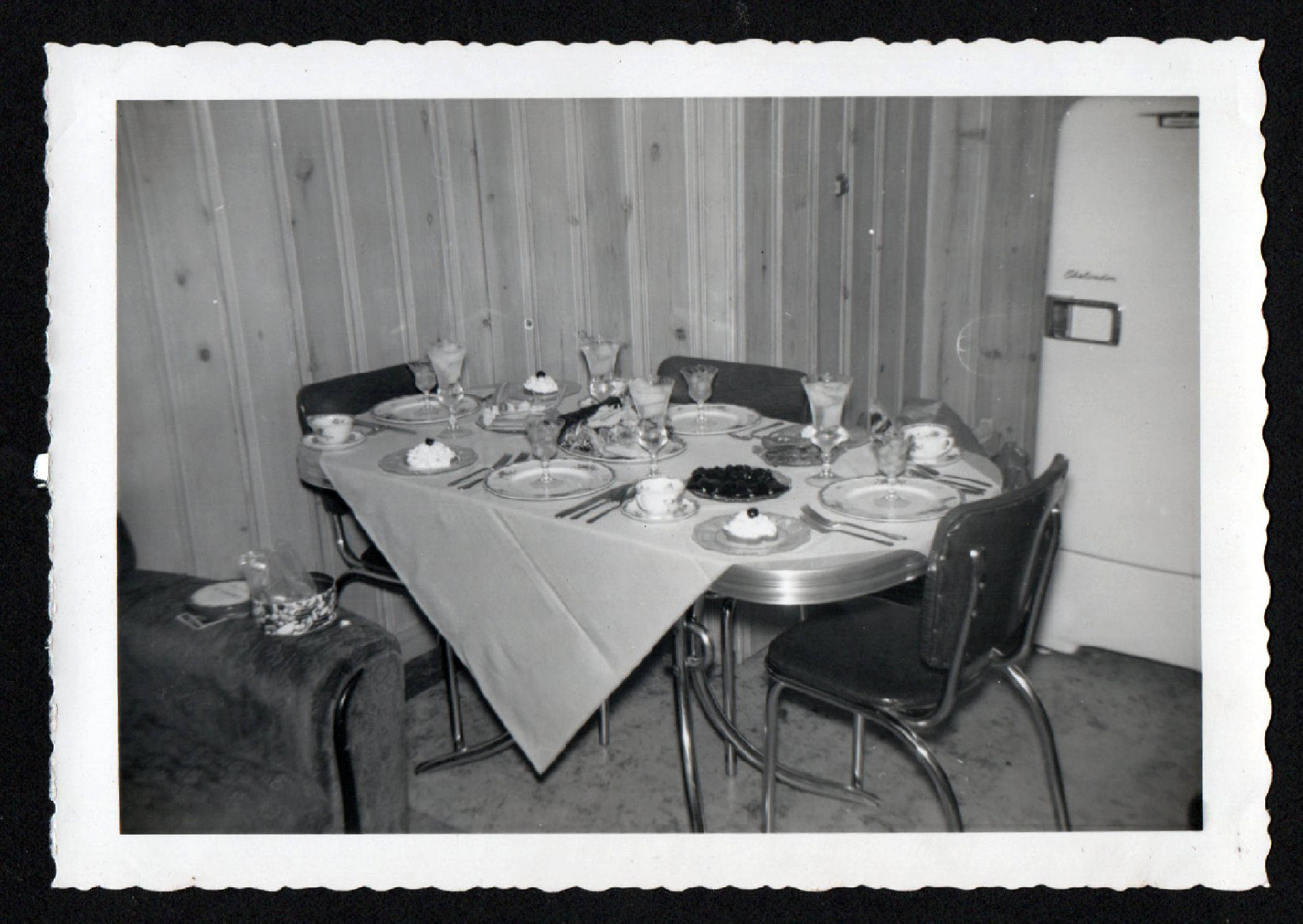 1950s Thanksgiving table set for dinner on a formica table in front of wood panneling wall and a 1950s fridge. 