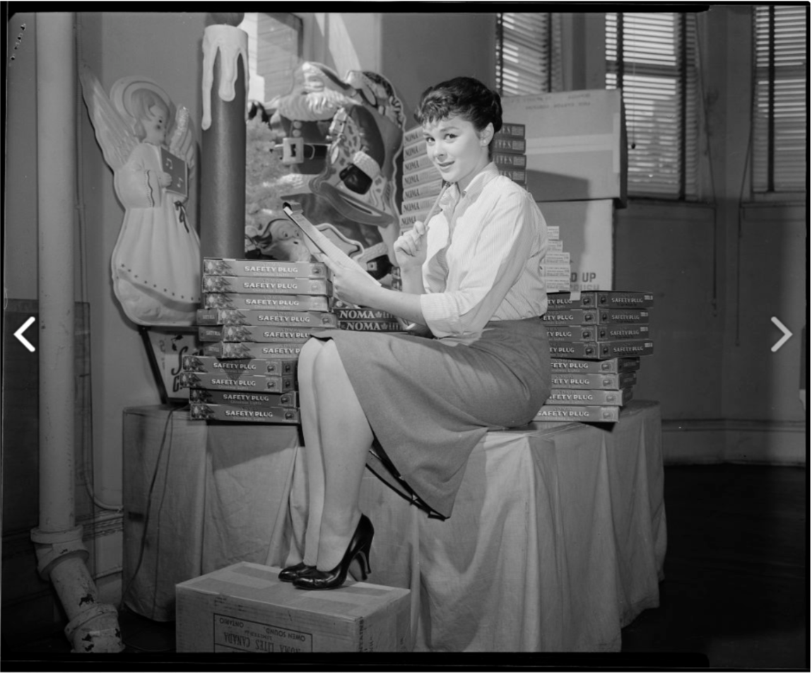 1950s vintage photo of a woman posing with Noma Christmas Lights in a room. She is about to do the Christmas Decorations. 