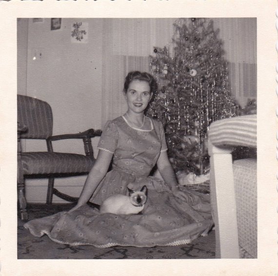 1950s vintage photo of a young woman in a 1950s dress posing in front of her Christmas Tree with her cat on her lap. -1956-