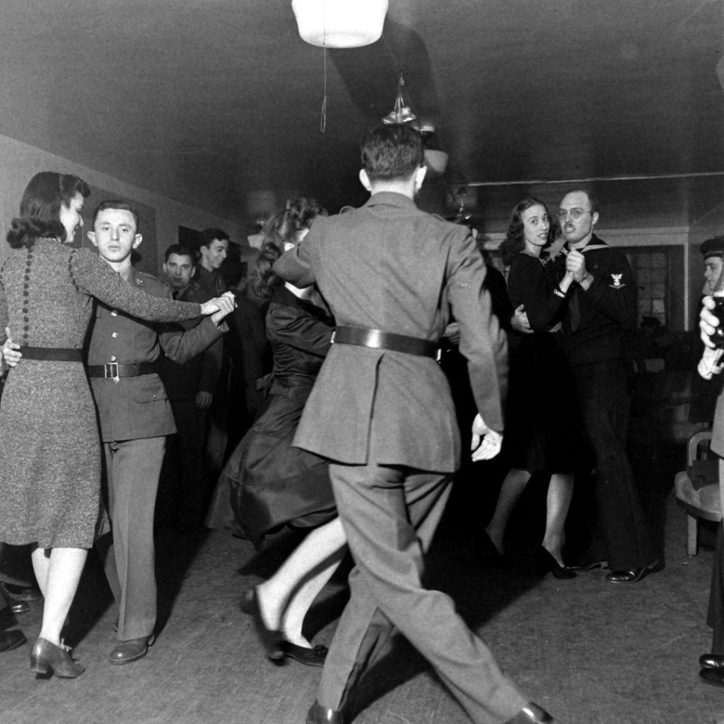 1940s vintage photo of a group of soldiers dancing in New York City on New Year's Eve, as 1941 turns to 1942. Super 1940s hairstyles on the women and 1940s dresses. 