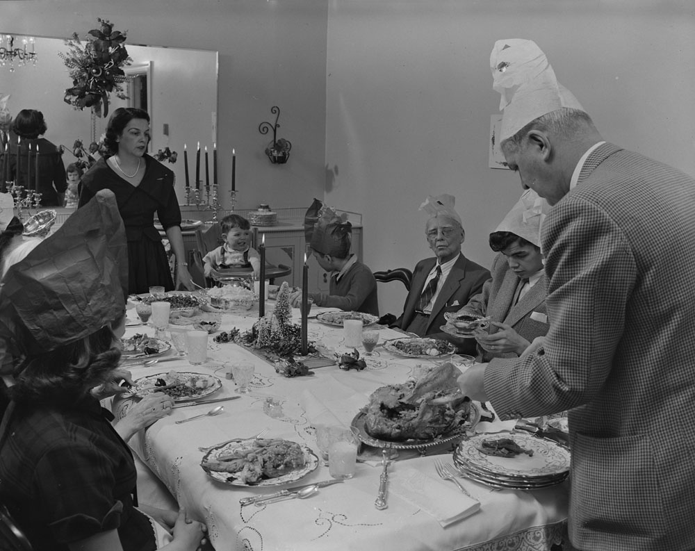 1950s vintage photo of a family with Christmas Cracker hats on their head at the Christmas dinner table-1959