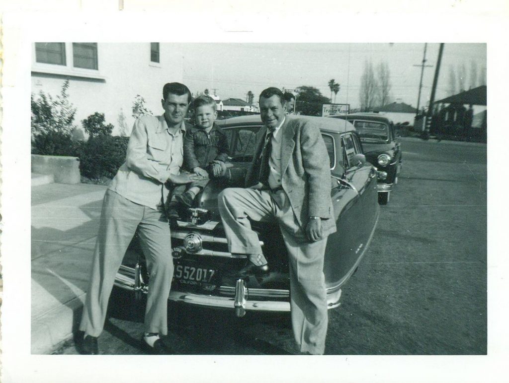 1950s vintage photo: 1952 photo of two men and a young boy in 1950s fashion sitting on a 1950s car.