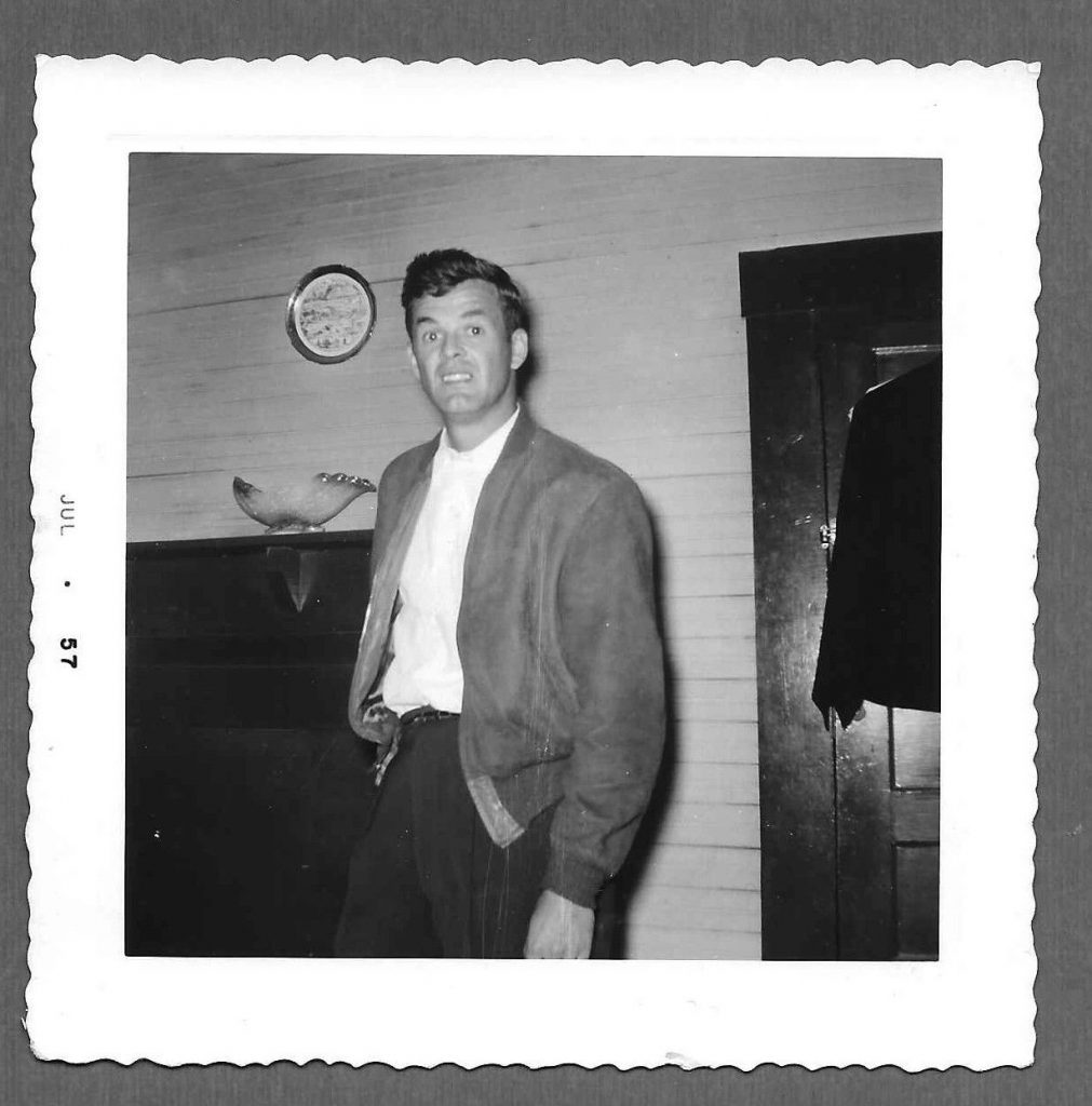 1950s vintage photo of a young handsome man in 1950s clothing standing in a 1950s room. 