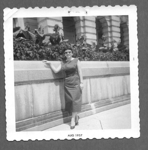 1950s vintage photo of a woman in a pencil skirt dress with cool 1950s sunglasses posing in front of a building. 