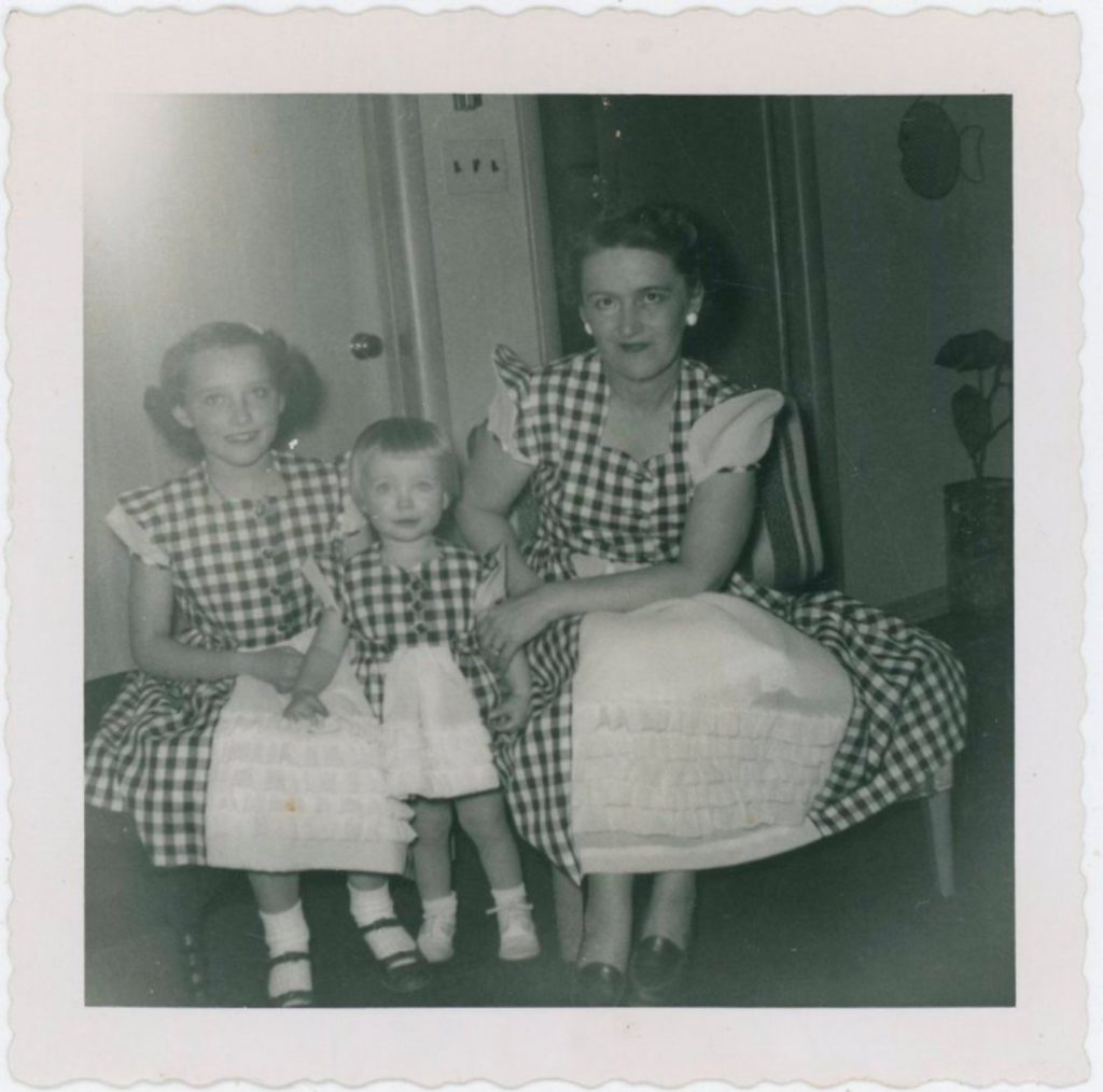 1950s vintage photo of a mother and her two childen in matching gingham dresses, 1954.