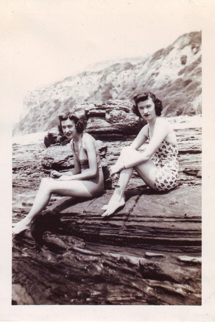 1943 Summer- 1940s Vintage Photo of two young women in 1940s hairstyles and 1940s swimsuits posing on a rock. Great 1940s Summer Fashion!