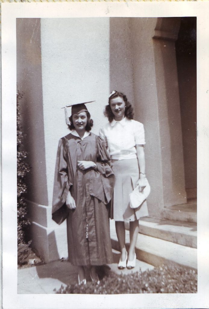 1940s vintage photo of 2 young women at a graduation. One is in a grad gown the other is in early 1940s fashions. June 1941. 