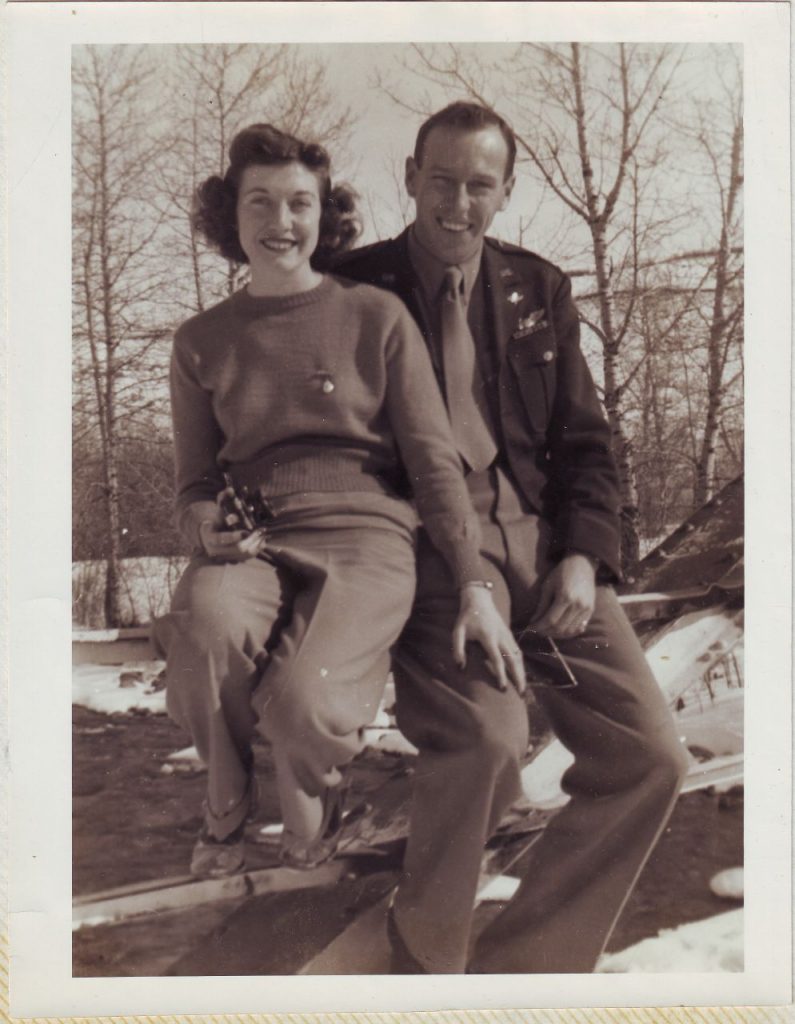 1940s vintage photo of a young married couple posing for a photo together in the winter. 1940s Hairstyle / 1940s fashions and WW2 uniform on display. 