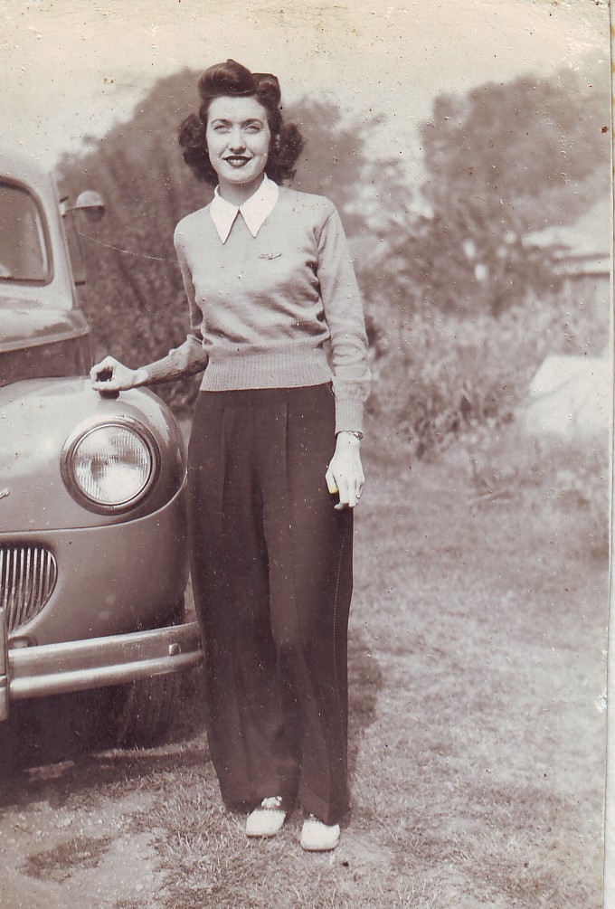 1940s vintage photo of a young woman (Doris) in 1940s fashion. She is wearing 1940s pants and sweater with blouse. Her hair is in 1940s Hairstyle. She is also posing beside a car and wearing saddle shoes. 