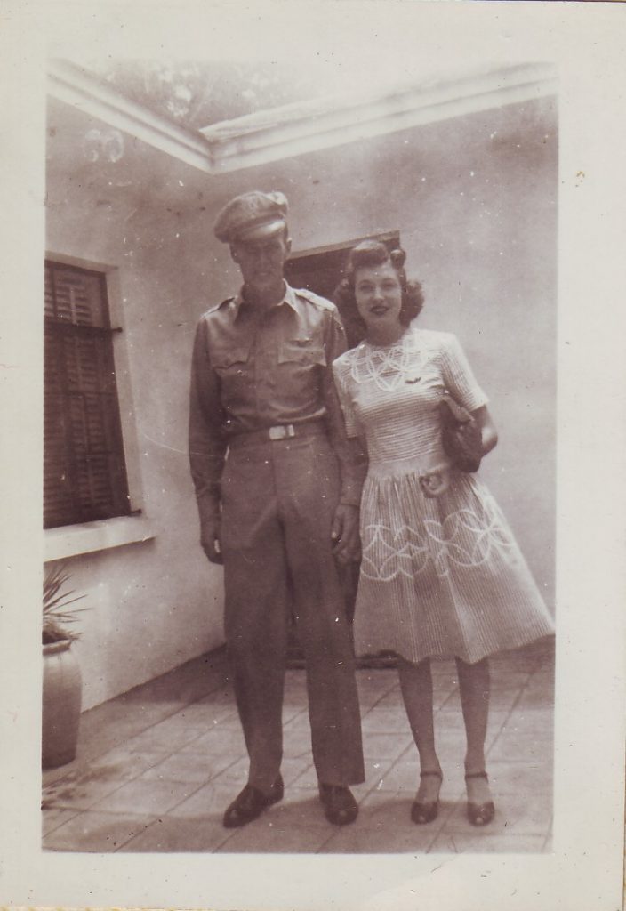 1940s Vintage photo of a man in uniform and young woman in a pretty 1940s dress and 1940s hairstyle posing together for a photo. 