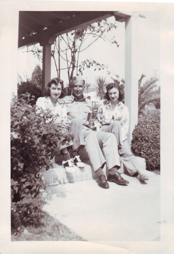 1940s photo of 2 women posing on a porch with a soldier in 1940s fashions and 1940s hairstyles. 