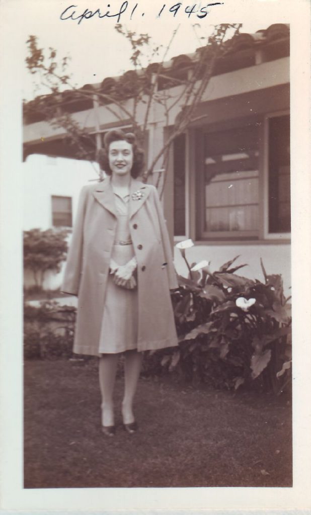 1940s vintage photo of a young woman in April 1945 with a 1940s hairstyle and 1940s fashion posing in front of her house. Super 1940s Coat. 