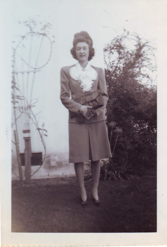 1940s photo of a woman in a 1940s 2 piece suit and 1940s hat and 1940s hairstyle. 