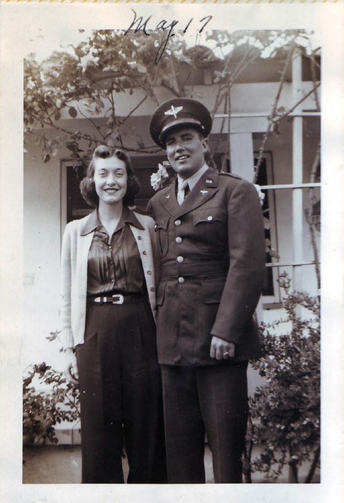 1940s photo of a young woman with a soldier. The woman is wearing 1940s hairstyle of Victory Roles and 1940s fashion of pants, blouse and cardigan. 