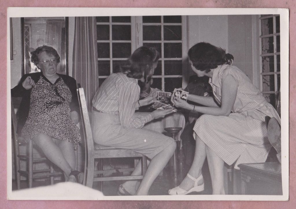 1940s photo of 2 young women looking at photos as grandmother sits nearby