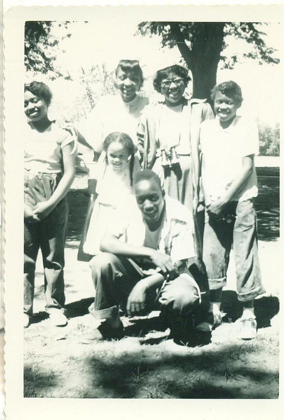 1950s vintage photo of a Black Grandma in the 1950s having a picture taken with all her grandchildren in the park. 