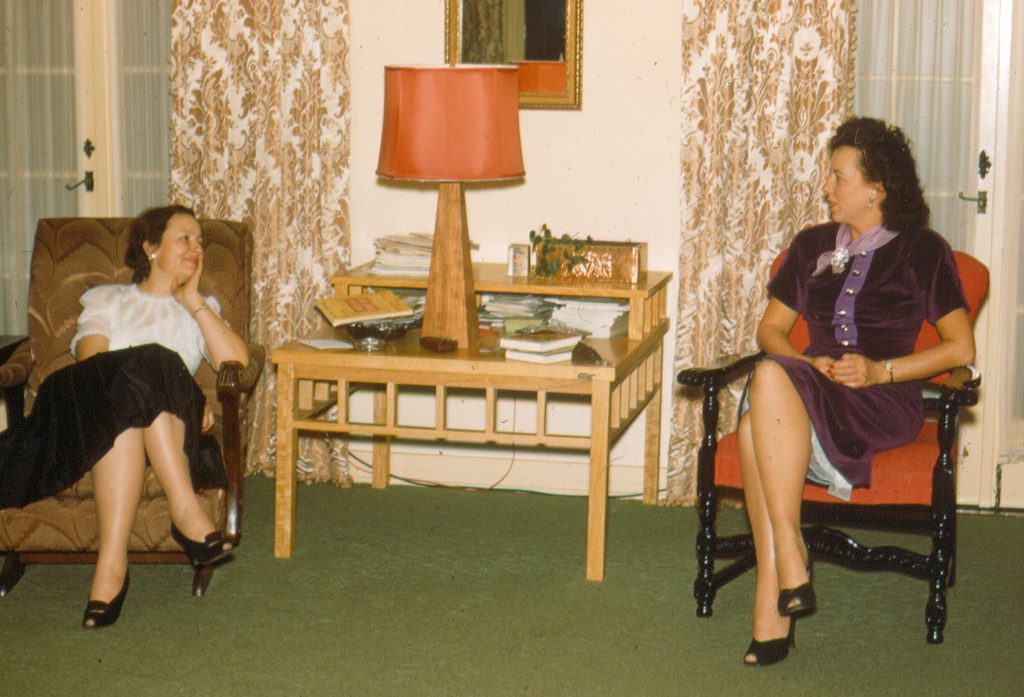 1950s vintage thanksgiving photo featuring two women in 1950s fashion 1950s in a Mid Century living room talking to each other. 