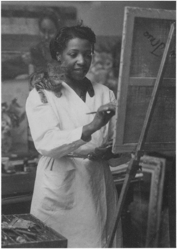 1930s vintage photo of Loïs Mailou Jones (1905-1998) painting in her Paris studio in 1937 or 1938 as her cat hangs out on her shoulder.