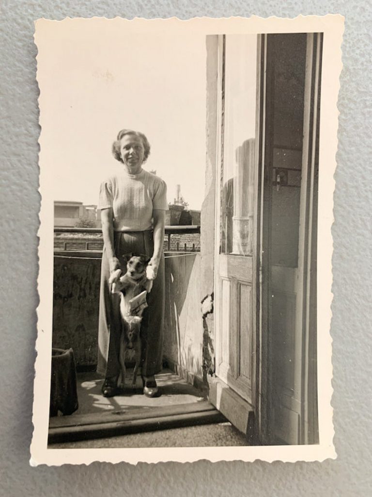 1940s photo of a woman holding her dog by its front paws for the photo. 