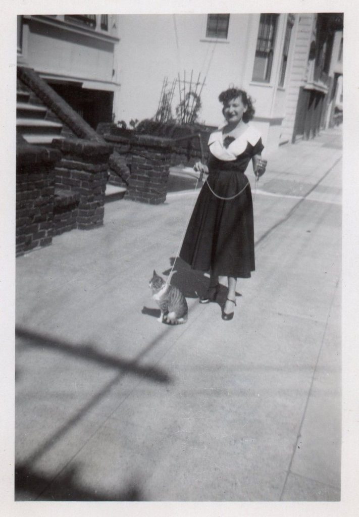 1950s photo of a woman with her pet cat going for a walk. The woman is wearing a 1950s dress. 