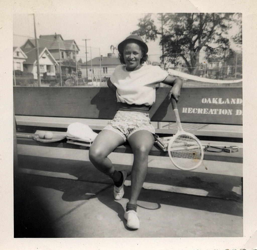 1950s Photo of a young Black woman sitting on a bench in her Tennis gear in Oakland, California.  Vintage Tennis Outfit Inspiration. 