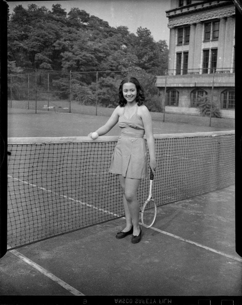 1940s Photo of a Black Women in a tennis outfit on the tennis court. Vivian V. Clayton, wearing two-piece tennis outfit, standing on tennis court holding tennis ball and racket