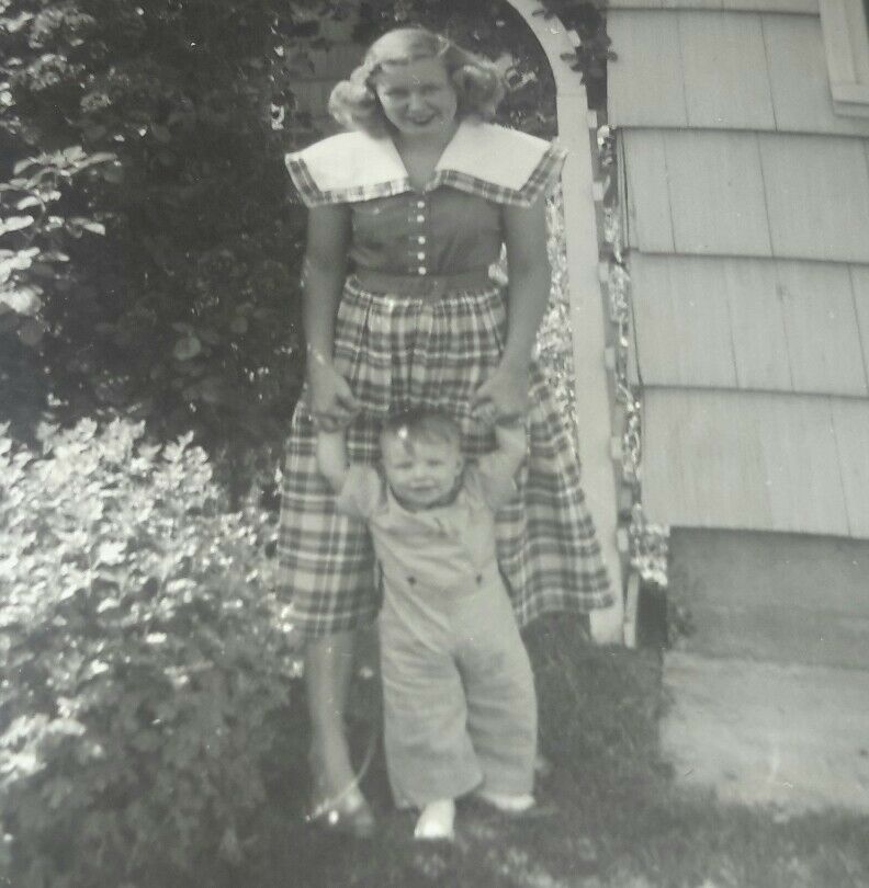 1950s Vintage Photo of a young mother in a plaid 1950s dress holding up her child. 