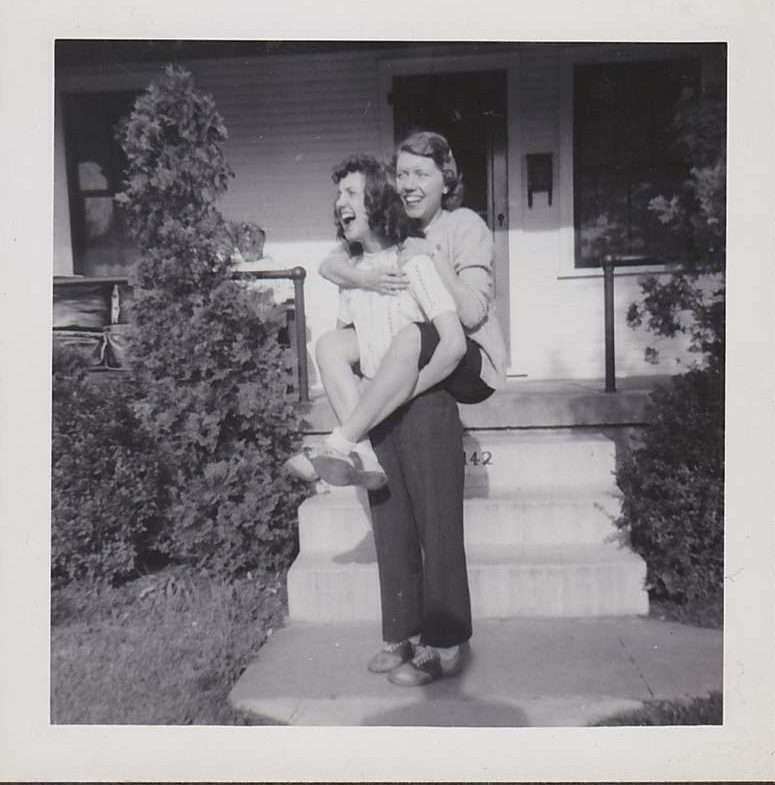 Late 1940s/ Early 1950s photo of 2 friends having fun in their saddle shoes with a piggy back ride. 