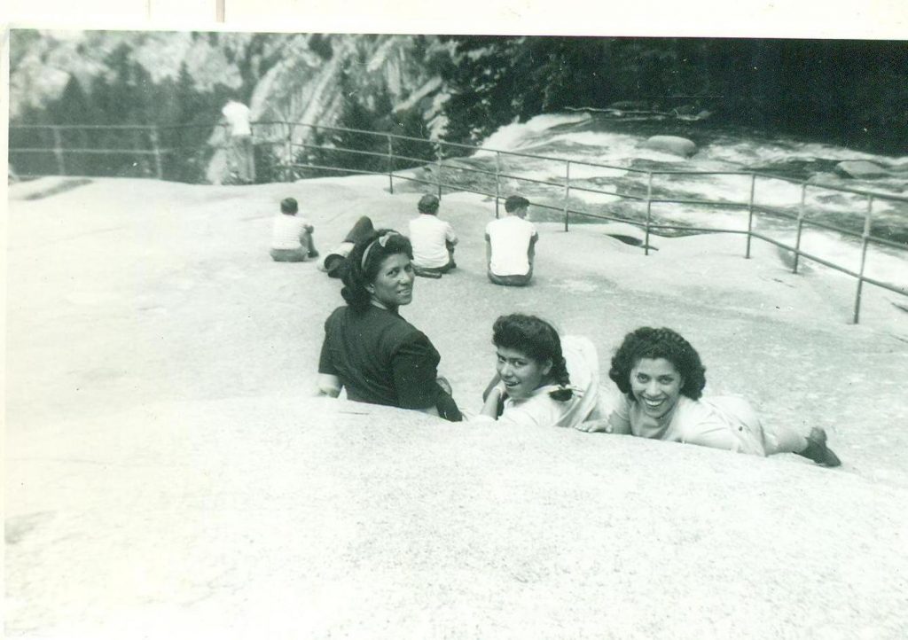 1940s photo of 3 young Black Women laying against a rock taking in the view of the top of a waterfall.