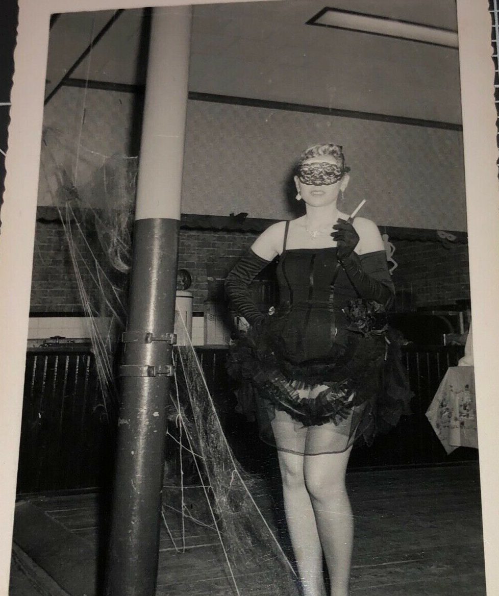 1950s photo of a woman in a sexy halloween outfit with masquerade mask on her face.