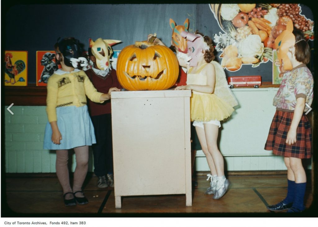 Image depicts a group of children in costume, with a carved pumpkin jack-o'-lantern, at a school Halloween event. 1950s vintage photo